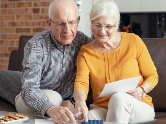 Un couple de seniors assis sur un canapé, examinant des documents et une carte bancaire pour planifier leur budget en résidence seniors.