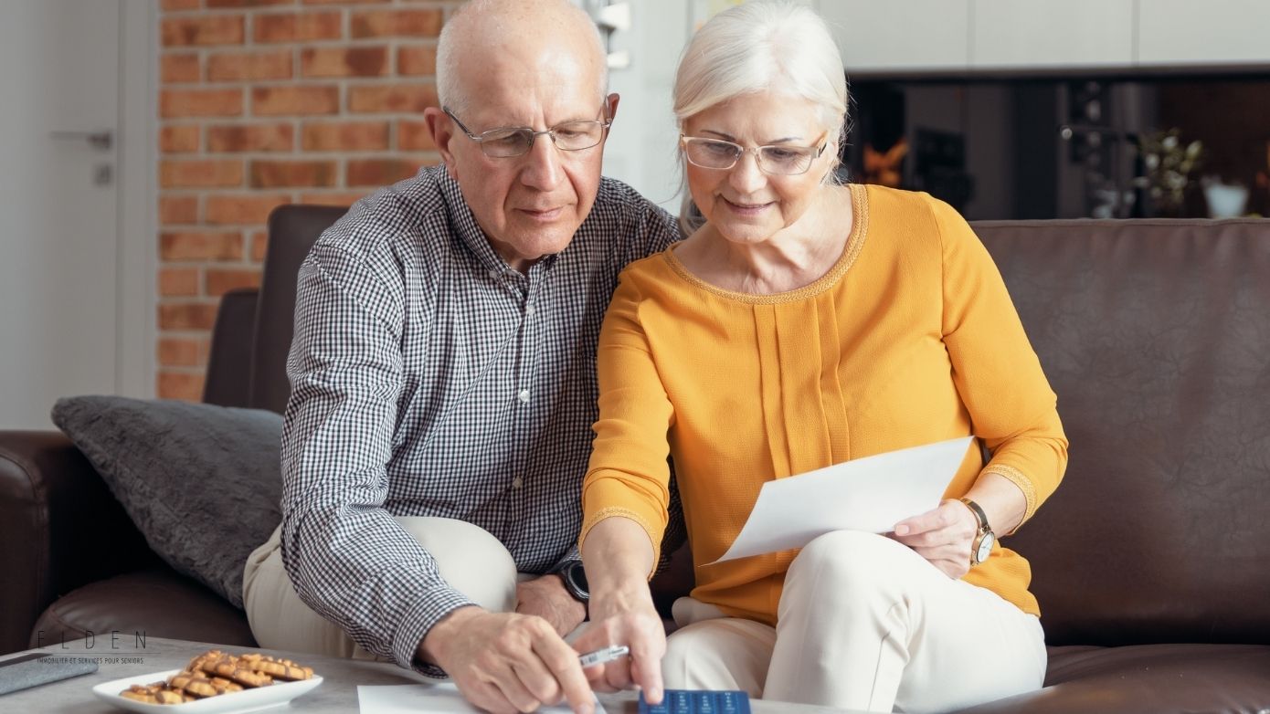Un couple de seniors assis sur un canapé, examinant des documents et une carte bancaire pour planifier leur budget en résidence seniors.
